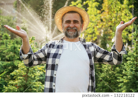Against automatic watering machine. Senior gardener is at work at daytime Against automatic watering machine. Senior gardener is at work at daytime 132218122
