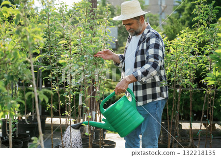 With watering can. Senior gardener is at work at daytime With watering can. Senior gardener is at work at daytime 132218135