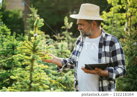 Black digital tablet in hand. Senior gardener is at work at daytime Black digital tablet in hand. Senior gardener is at work at daytime 132218164
