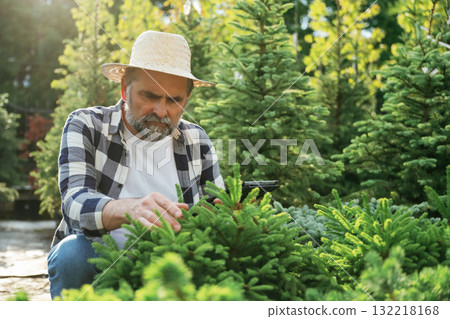 Black digital tablet in hand. Senior gardener is at work at daytime Black digital tablet in hand. Senior gardener is at work at daytime 132218168