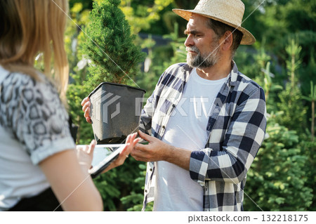 Taking a plant in a pot. Woman and man are working in the garden together with plants 132218175