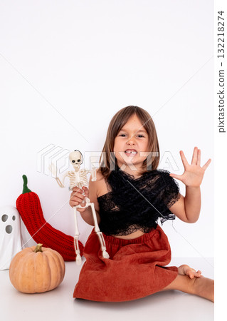 Caucasian female child in Halloween costume holding skeleton with pumpkin and decorations with copy space for text 132218274