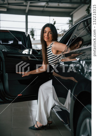 Going out the door. Beautiful young woman is with new automobile in car showroom 132218315
