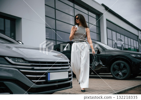 With white cup of drink. Attractive young woman is outdoors near her brand new car 132218335