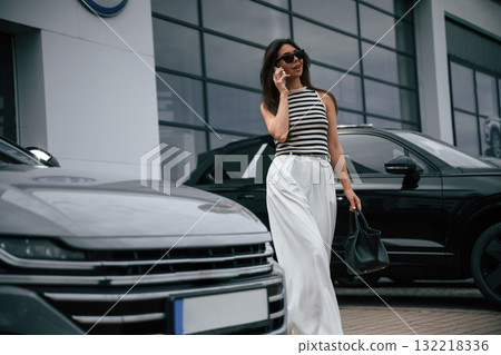 Talking by phone. Attractive young woman is outdoors near her brand new car 132218336