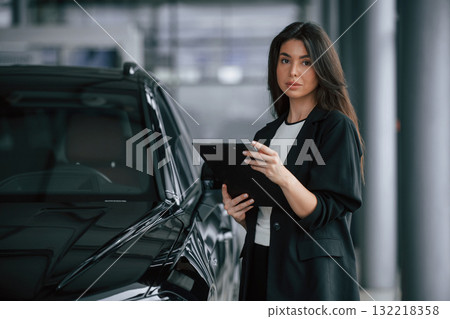 Notepad in hands. Saleswoman in car showroom, selling automobile Notepad in hands. Saleswoman in car showroom, selling automobile 132218358