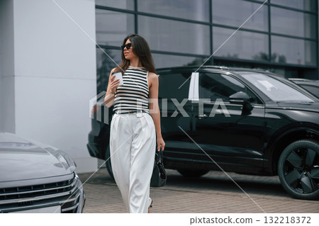 Walking holding drink. Attractive young woman is outdoors near her brand new car 132218372