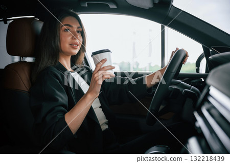 White cup of fresh drink in hand. Beautiful businesswoman is in the new car White cup of fresh drink in hand. Beautiful businesswoman is in the new car 132218439