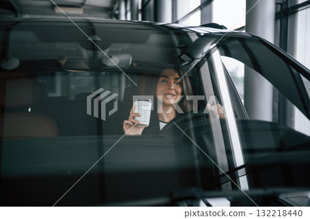 White cup of fresh drink in hand. Beautiful businesswoman is in the new car White cup of fresh drink in hand. Beautiful businesswoman is in the new car 132218440