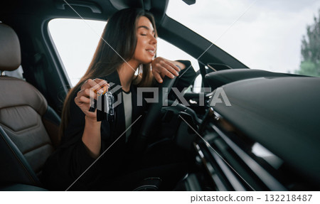 Black colored keys of new automobile. Beautiful businesswoman is in the new car Black colored keys of new automobile. Beautiful businesswoman is in the new car 132218487