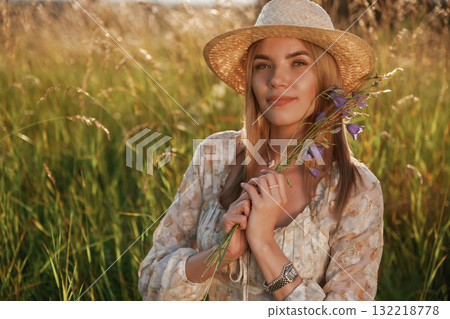 In straw hat, with plant in hands. Beautiful young woman is on the field, countryside 132218778