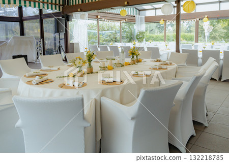 Elegant wedding reception table set for guests with floral decor and place settings. White chairs surround the circular table adorned with yellow and white flowers, lemons, and name cards 132218785
