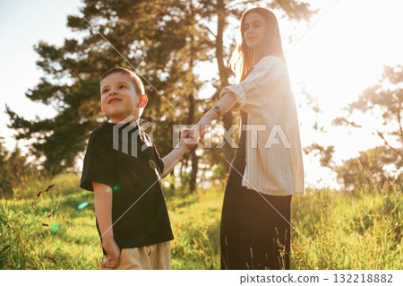 Holding each other by a hands. Mother and son are in the forest together Holding each other by a hands. Mother and son are in the forest together 132218882