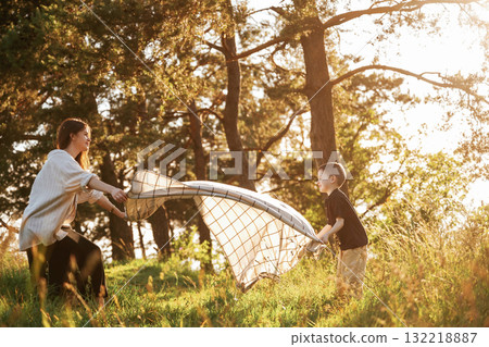 With blanket, putting it on the ground. Mother and son are in the forest together With blanket, putting it on the ground. Mother and son are in the forest together 132218887
