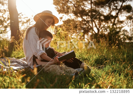Sitting and reading the book. Mother and son are in the forest together Sitting and reading the book. Mother and son are in the forest together 132218895