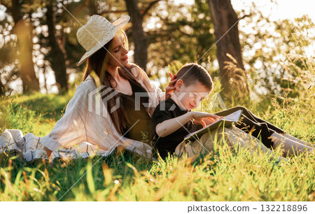 Sitting and reading the book. Mother and son are in the forest together Sitting and reading the book. Mother and son are in the forest together 132218896