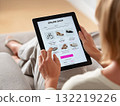 A person explores an online shop on a tablet while sitting comfortably on a couch 132219226