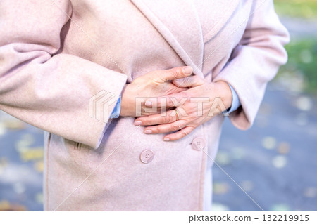 Elderly woman clutching her abdomen in pain, grimacing from cramps or indigestion, experiencing discomfort and digestive distress at home, senior health and illness concern 132219915