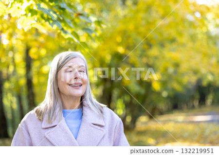 Senior woman relaxing with closed eyes in autumn park, feeling tranquil and peaceful during a sunny day surrounded by golden trees, enjoying retirement and a healthy lifestyle Senior woman relaxing with closed eyes in autumn park, feeling tranquil and peaceful during a sunny day surrounded by golden trees, enjoying retirement and a healthy lifestyle 132219951
