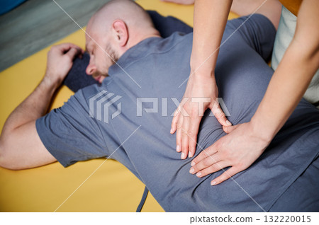 Masseuse making thai yoga massage. Therapist doing traditional massage treatment for male patient indoors. Bald client lying on mat, meditating, enjoying hand massage in calm atmosphere. 132220015