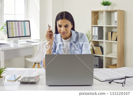 Young business woman accountant working on a laptop computer with tables at office. 132220107