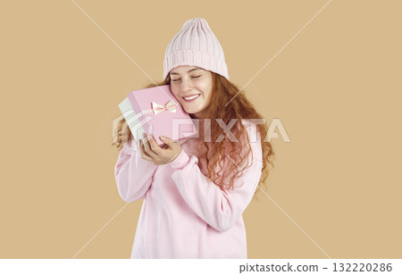 Happy young woman in warm pastel pink winter clothes holding gift box and smiling 132220286