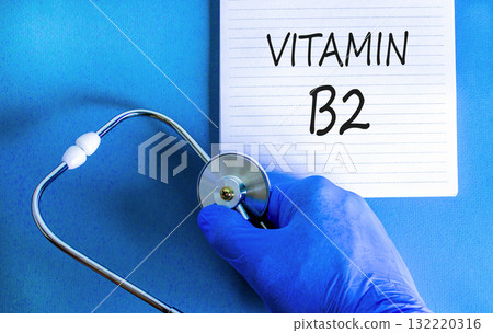 Vitamin B2 riboflavin symbol. Concept words Vitamin B2 on beautiful white note. Doctor's hand in blue medical glove. Beautiful blue background. Medical healthy lifestyle Vitamin B2 riboflavin concept. 132220316