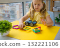 On a yellow background, a little girl is playing with magnetic construction pieces. 132221106