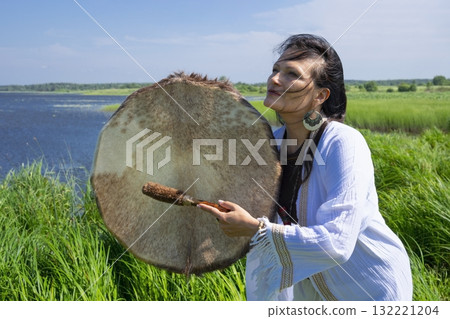 Female shaman in the white dress drumming outdoors Female shaman in the white dress drumming outdoors 132221204