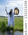 Shaman in the white dress drumming in the natural environment 132221206