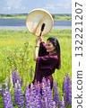 Shaman woman drumming among blooming flowers in summer 132221207