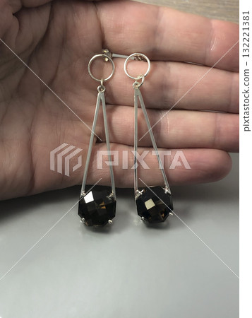 Elegant silver earrings with black faceted stones held in a hand against a light 132221381