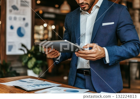 A man in a suit is holding a tablet and looking at a presentation 132224813