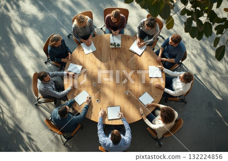 Diverse Group Engaged in Collaborative Meeting Around Round Table in Modern Office 132224856