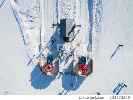 Skiers and snowboarders preparing to ascend the slopes at a winter resort in a snow-covered landscape during a sunny day. 132225239