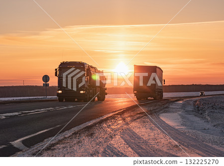 Two large trucks navigate a snowy highway at sunset Two large trucks navigate a snowy highway at sunset 132225270