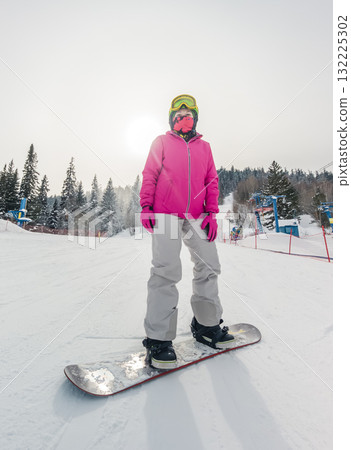 A snowboarder stands on a snowy slope, dressed in a vibrant pink jacket and goggles A snowboarder stands on a snowy slope, dressed in a vibrant pink jacket and goggles 132225302