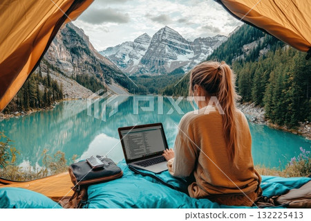 Scenic Working Retreat in Nature: Young Woman Using Laptop Inside Tent by Lake with Majestic Mountain View and Lush Forest Surroundings Scenic Working Retreat in Nature: Young Woman Using Laptop Inside Tent by Lake with Majestic Mountain View and Lush Forest Surroundings 132225413