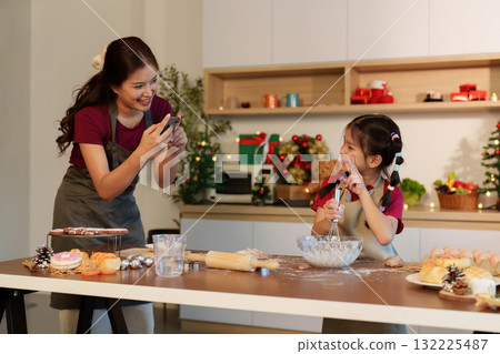 Creative baking moments. Mother capturing joyful memories with daughter in festive kitchen. 132225487