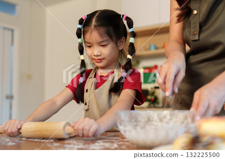 Baking Together. Young girl rolling dough with her mother in a festive kitchen. Baking Together. Young girl rolling dough with her mother in a festive kitchen. 132225500
