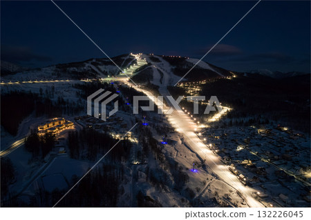 Winter night view of illuminated ski slopes and a village in a mountainous region 132226045