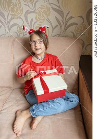 A girl in a Santa Claus hat opens a gift. It's Christmas time. 132226069