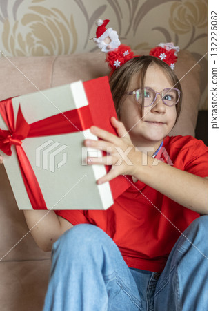 A girl in a Santa Claus hat opens a gift. It's Christmas time. 132226082