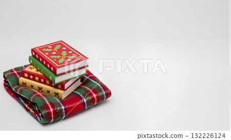 Christmas Reading. A stack of holiday books on a folded checkered blanket against a white background. Christmas Reading. A stack of holiday books on a folded checkered blanket against a white background. 132226124
