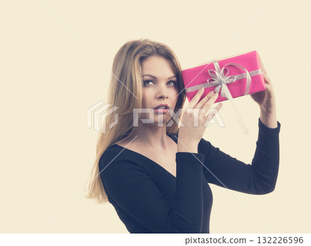 Girl holding present shaking pink gift box Girl holding present shaking pink gift box 132226596