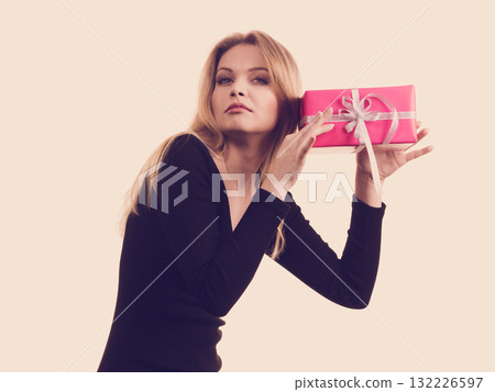 Girl holding present shaking pink gift box 132226597