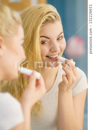 Woman in bathroom applying lip balm Woman in bathroom applying lip balm 132226651