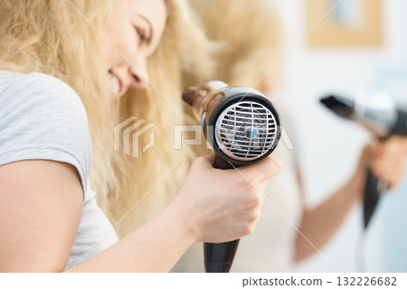 Blonde woman using hair dryer Blonde woman using hair dryer 132226682