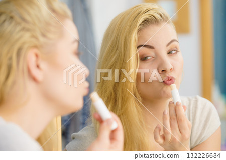 Woman in bathroom applying lip balm 132226684