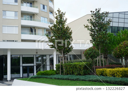 A modern residential building with landscaped greenery and well-maintained trees in front A modern residential building with landscaped greenery and well-maintained trees in front 132226827
